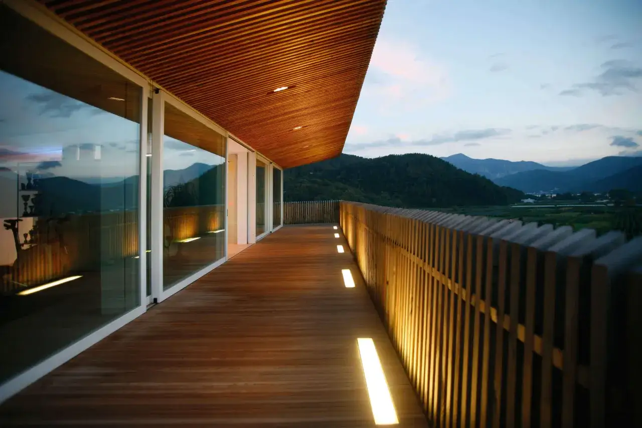 Un moderno terrazzo in legno con luci integrate lungo la balaustra e sotto la tettoia, perfetto per capire come illuminare un terrazzo con stile.