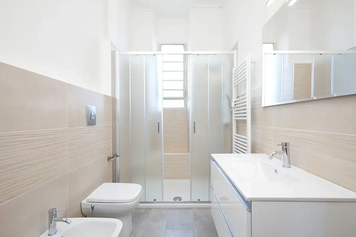 Un bagno moderno con doccia in vetro, lavabo bianco e bidet. Le pareti sono piastrellate in tonalità neutre.