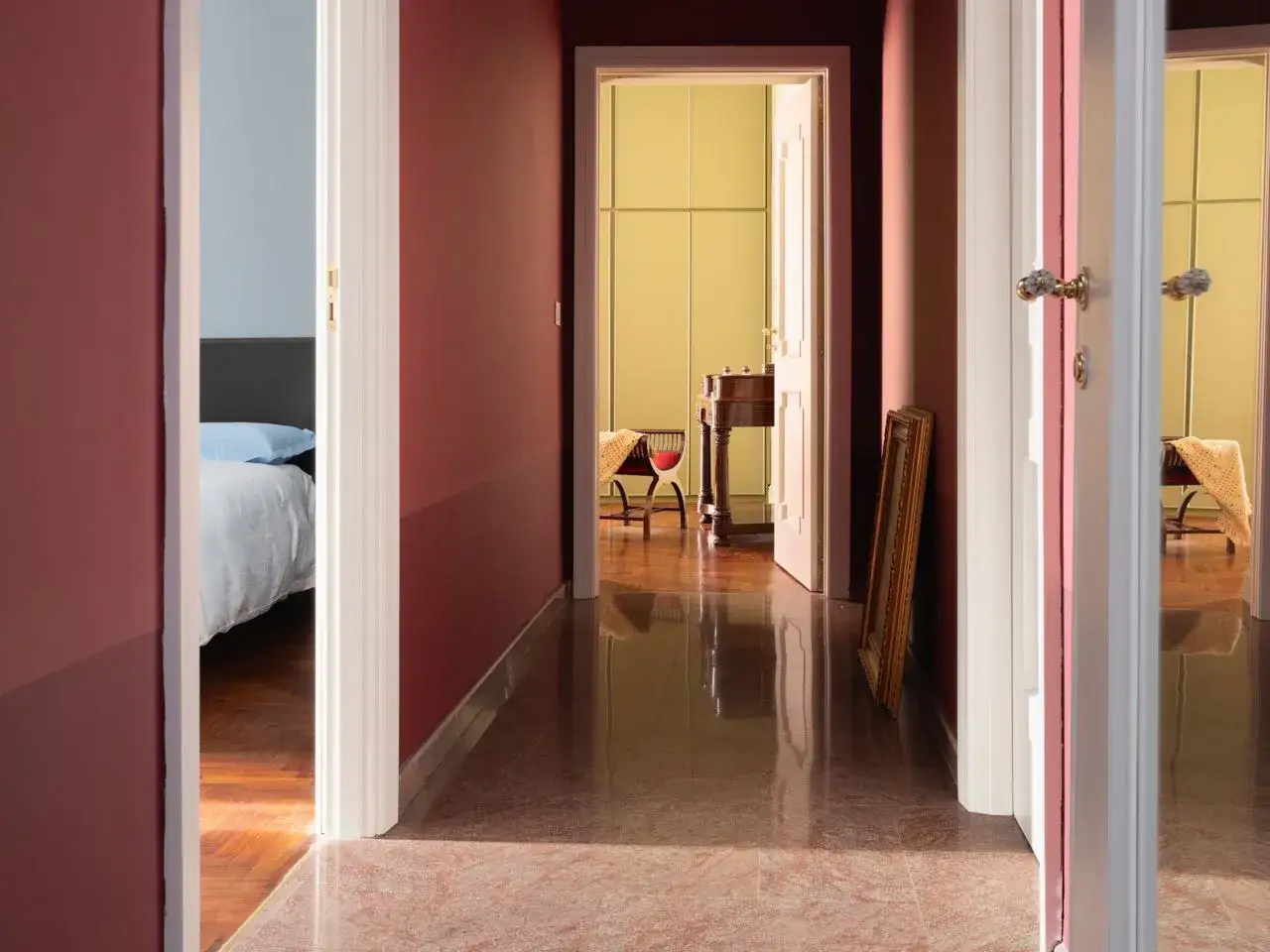 Corridoio con pareti bordeaux e giallo pallido, che suggeriscono idee per i colori per ingresso e corridoio. Pavimento in marmo rosa.