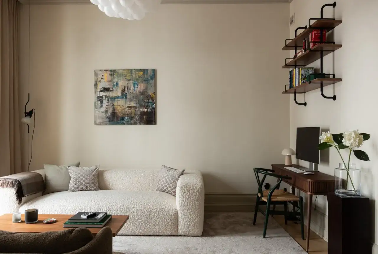 Soggiorno moderno con divano boucl&eacute; bianco, tavolino in legno e un quadro astratto. Le pareti colore crema creano un'atmosfera calda e accogliente.