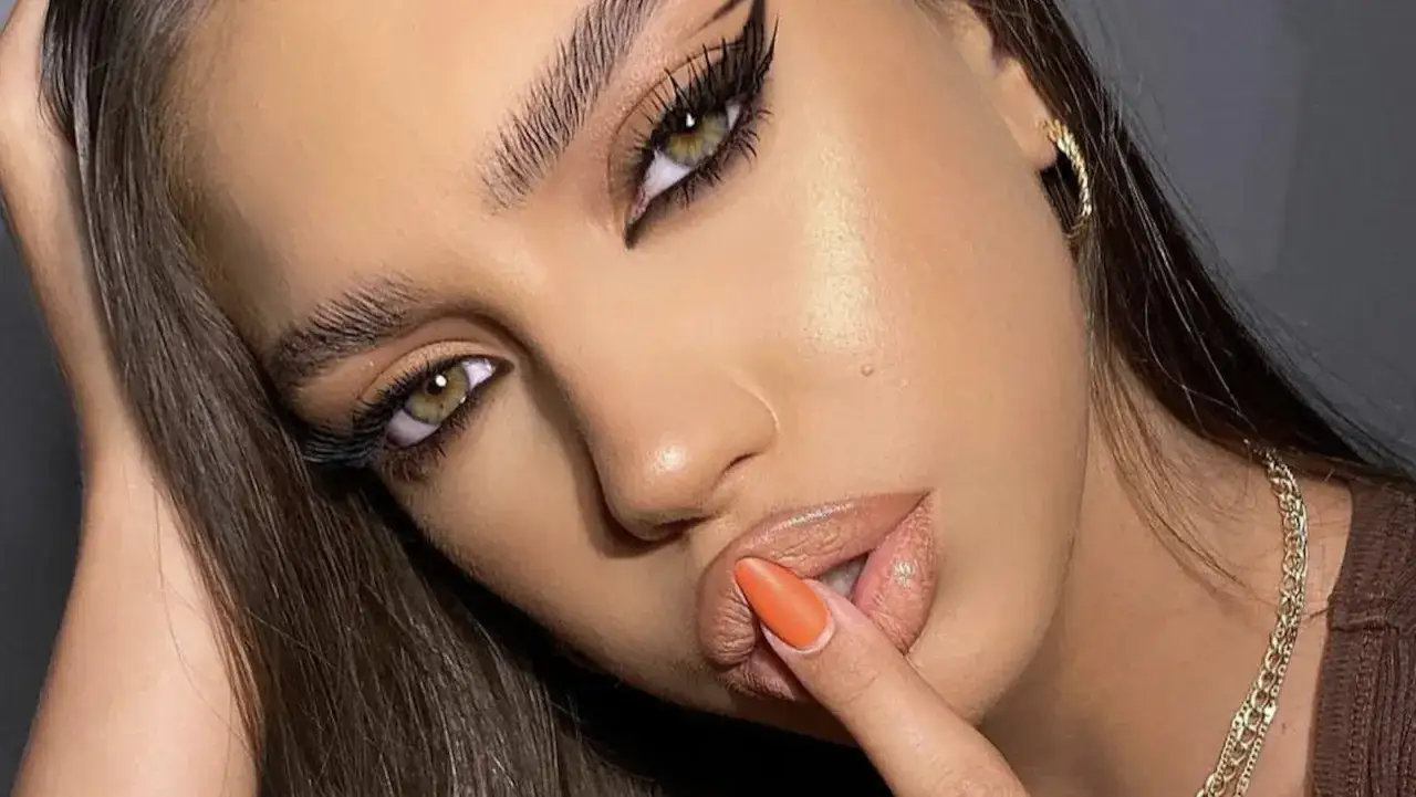 Occhi da sirena con eyeliner grafico e ciglia lunghe, labbra carnose e unghia arancione.