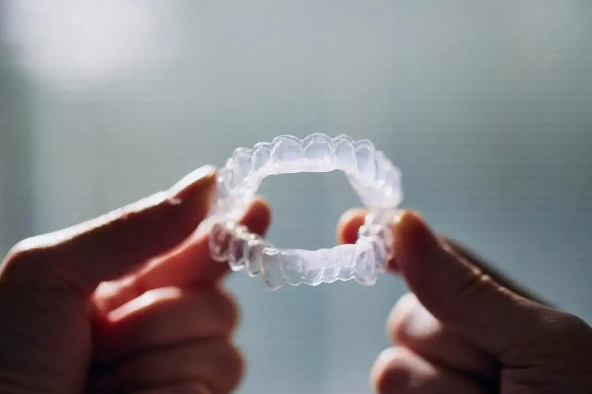 Mani tengono un apparecchio trasparente, utile per lo sbiancamento denti pro e contro.