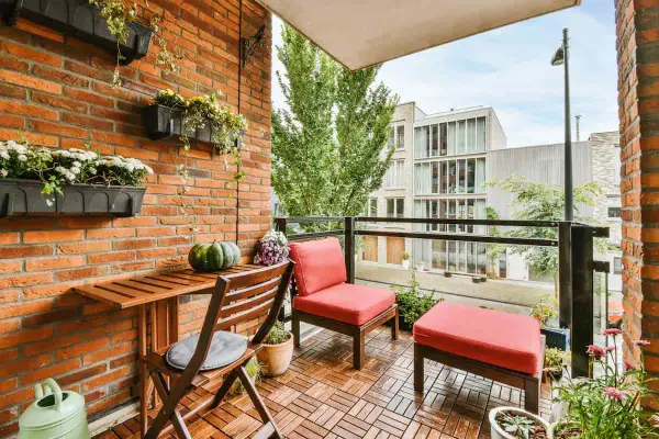 Arredare terrazzo appartamento: un angolo relax con sedie rosse, tavolino in legno e piante su muro di mattoni.