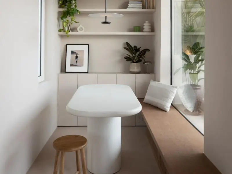 Un angolo accogliente con tavolo bianco, sgabello in legno e piante. Un'ispirazione su come combattere la solitudine in casa, creando spazi piacevoli.