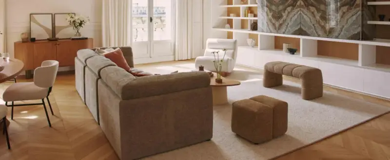 Soggiorno con divano componibile, poltrona, pouf e panca. Arredamento casa stile moderno con mobili in legno e tessuti neutri.